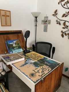 Room with a jigsaw puzzle table featuring a puzzle, cross on the wall, and lamp.