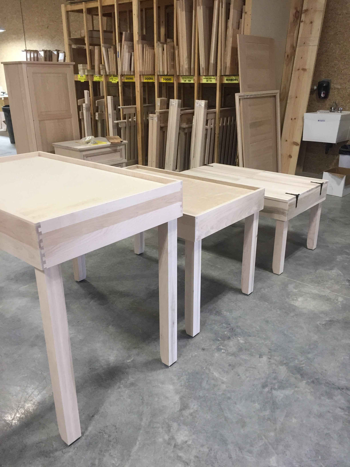 Wooden jigsaw puzzle tables in a workshop setting with wooden planks and panels in the background.