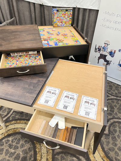 jigsaw puzzle tables displayed with drawers open to reveal the jigsaw puzzle pieces and the split open tabletops open on the right side to reveal the on going jigsaw puzzle